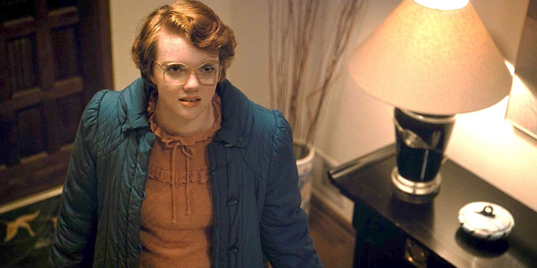 Shannon Purser jako Barbara Holland, okulary i niebieski płaszcz, w przedpokoju.